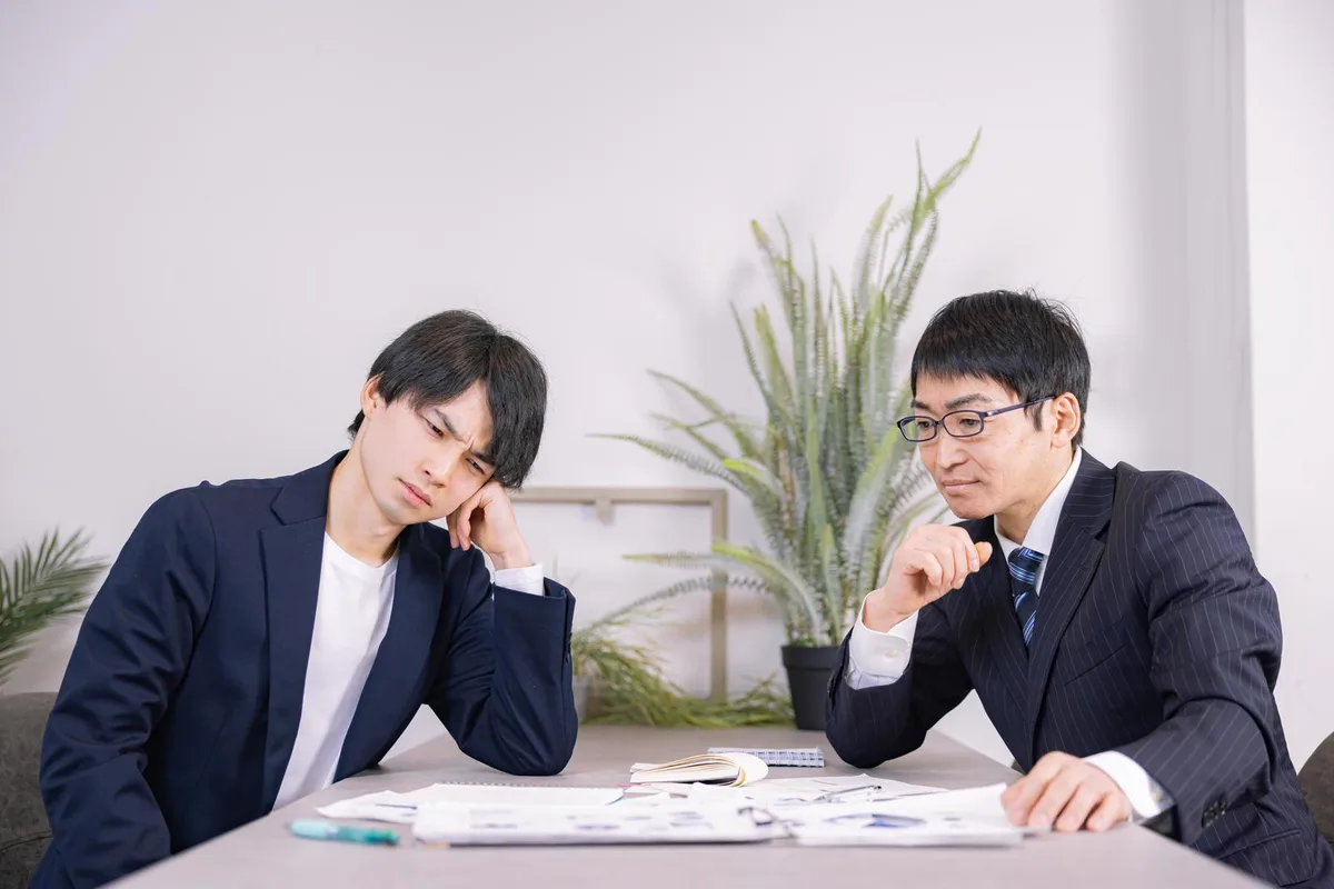 資料を前に考え込む2人の会社員の打ち合わせ